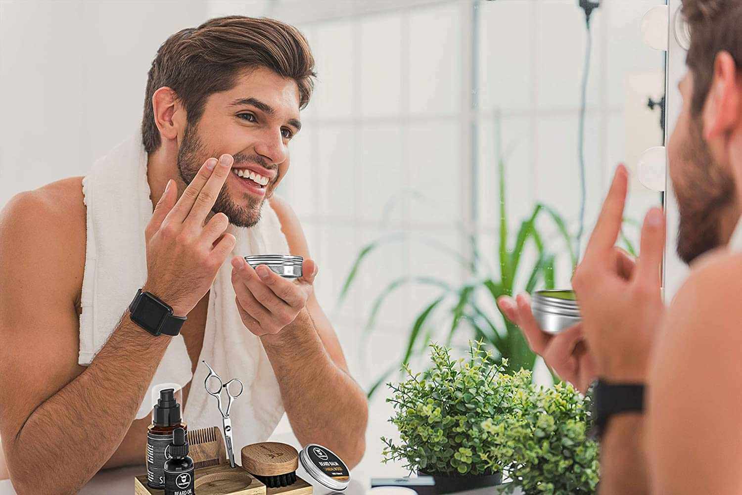 Man applying beard balm from Beard Kit with Caddy in front of mirror, surrounded by grooming accessories.