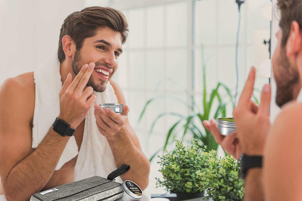 Man using beard grooming kit in front of mirror with toiletries and plants.