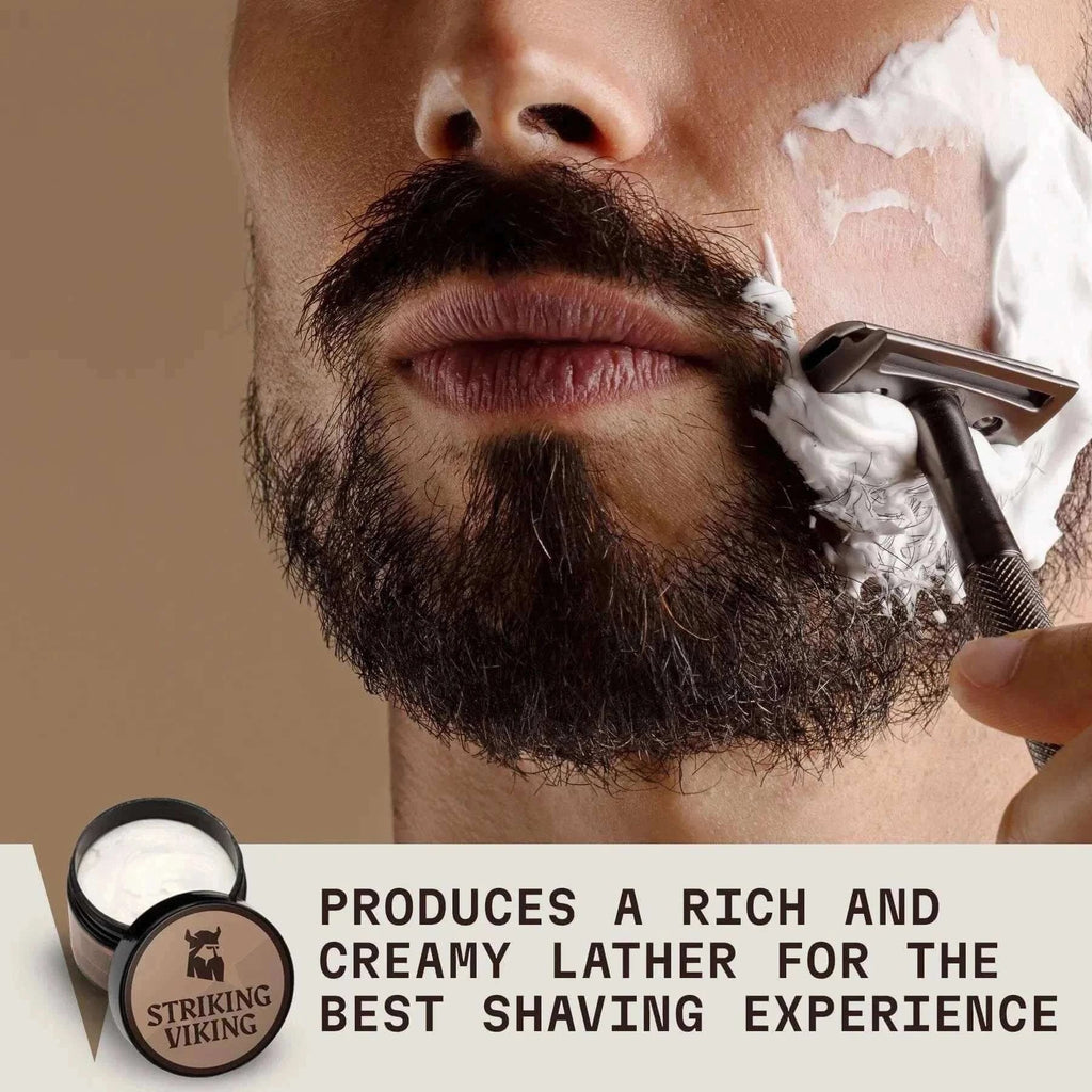 Shaving cream being applied to a man's beard with a brush, next to a Striking Viking Sandalwood Shaving Cream tub, promoting rich and creamy lather for men's shaving.